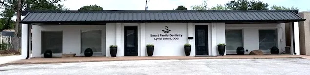 Photo of the exterior of Smart Family Dentistry, a modern white building with a black roof and potted plants at the entrance.